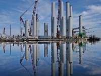 Two men walk across the bridge to the dock in front of the wind turbine towers for the Vineyard Wind offshore wind farm being assembled at the New Bedford Marine Commerce Terminal.