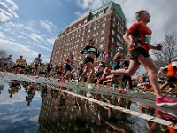 Runners are reflected in a puddle, as them make their way up Pleasant Street during the 2024 New Bedford Half Marathon on March 17, 2024.