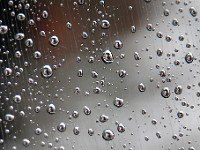 A man walking up Purchase Street with an umbrella in hand is reflected on the rain drops of a window, on a rainy morning.