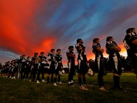 The sun sets in the distance as Apponequet Regional High School players listen to the National Anthem before playing Dartmouth High School on Friday night football.