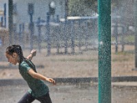 A girl runs through the fine water mist thrown up by the sprinklers at Clasky Common Park in New Bedford on a sweltering day.