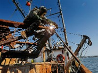 Chris Macedo of Macedo Welding finds himself perched atop a dredge as he makes repairs to the skid plats of the sea clam fishing boat docked in New Bedford