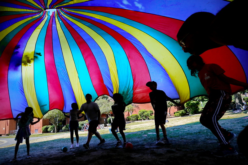 Kids attending Camp Frederick Douglass at the YMCA in downtown New Bedford, MA have some fun sliding under the colorful parachute.  PHOTO PETER PEREIRA