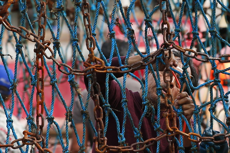 A fisherman aboard the scalloper Ian Nigel uses a needle to make repairs to the netting on one of the fishing boat's dredges while docked in New Bedford, MA. PHOTO PETER PEREIRA