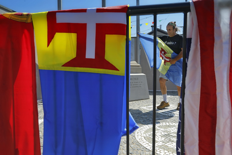 Joe Aguiar removes the weathered flag of the Portuguese island of Madeira, in preparation to replace it along with the Portuguese flag, left and American flag, right with new ones for the grand opening of the Feast of the Blessed Sacrament in New Bedford, MA. PHOTO PETER PEREIRA