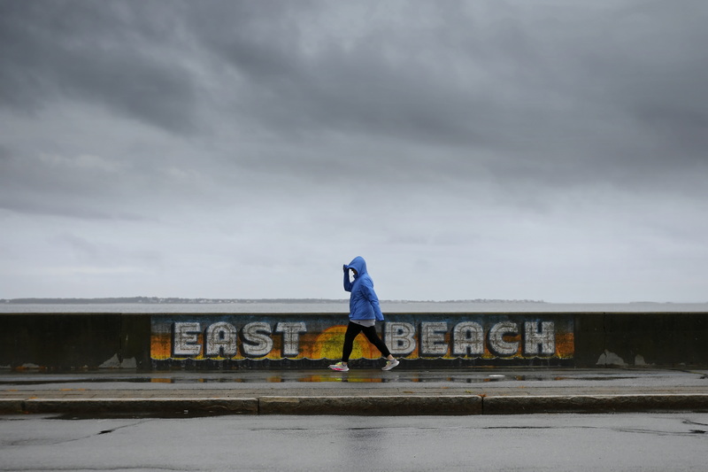 A woman walks past the East Beach sign painted on the retaining wall on East Rodney French Boulevard in New Bedford, MA on a rainy day. PHOTO PETER PEREIRA