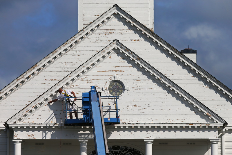 A painter scrapes the existing paint from the facade of St. Mary's Parish in Dartmouth, MA before repainting the church. PHOTO PETER PEREIRA