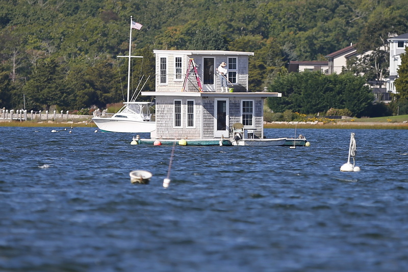 A man is seen sweeping the deck of a small houseboat anchored in the middle of Padanaram harbor in Dartmouth, MA. PHOTO PETER PEREIRA