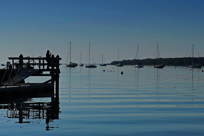 A woman enjoys a cup of coffee on a pier overlooking Mattapoisett harbor shortly after sunrise. PHOTO PETER PEREIRA