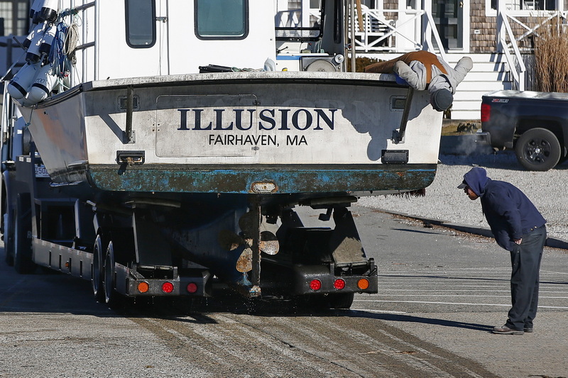 Two men take a closer look at the hull of the lobster boat Illusion, after pulling it out of the water in Mattapoisett, MA.  PHOTO PETER PEREIRA