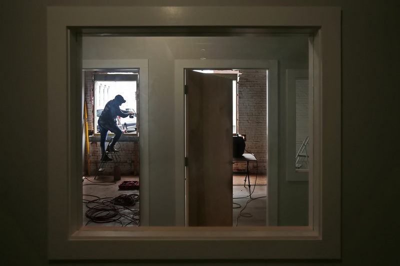 Rodrigo Sobral is framed by various indoor windows and door frames, as he installs new exterior windows on an office building being remodeled on N Water Street in downtown New Bedford.