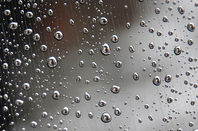 A man walking up Purchase Street in New Bedford, MA with an umbrella in hand, is reflected on the rain drops of a window, on a rainy morning. PHOTO PETER PEREIRA