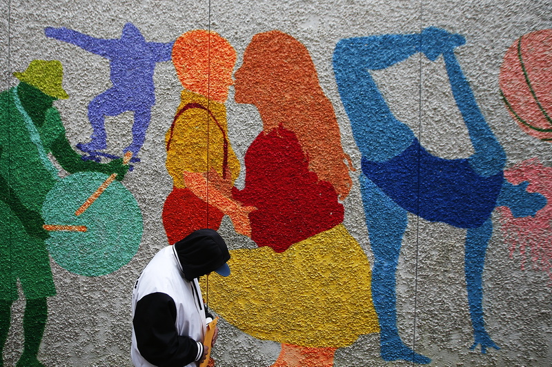 A man walks past the colorful figures painted on the wall of the Sears Court connector in downtown New Bedford, MA.  PHOTO PETER PEREIRA