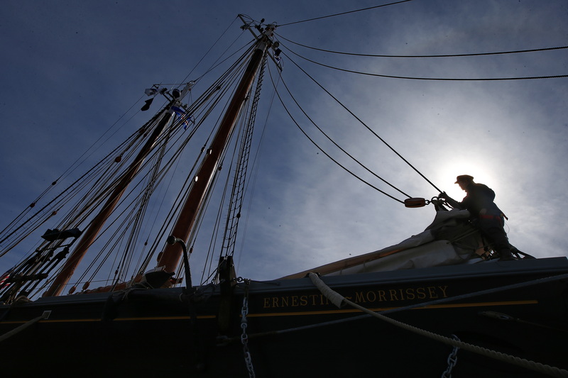 Harper McDonald is framed by the rising sun as he installs the attachments for the jumbo sail on the stern of the Ernestina-Morrissey schooner docked in New Bedford, MA.  PHOTO PETER PEREIRA