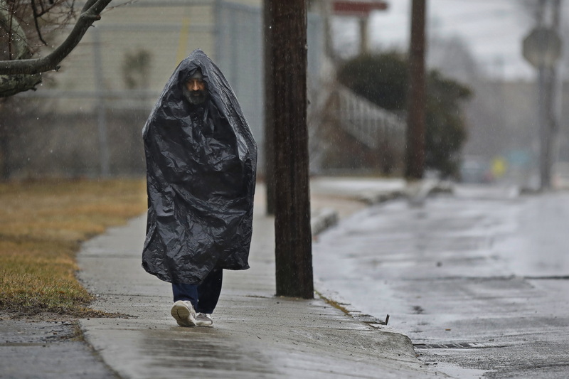 A man uses a large plastic bag to take shelter from the driving rain as he makes his way down S Front Street in New Bedford, MA. PHOTO PETER PEREIRA