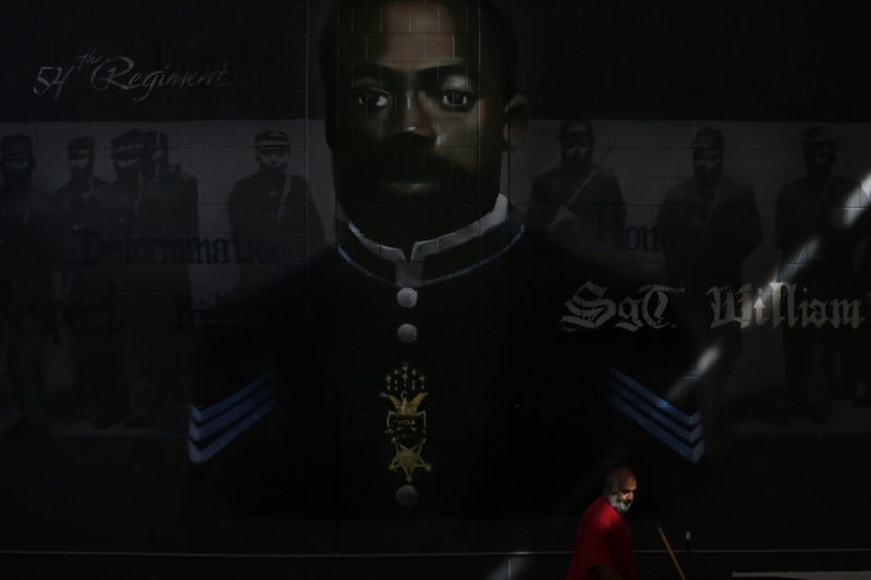 A man is illuminated by a ray of light coming from the windows above, as he makes his way across a mural of Carney Academy's namesake SGT William H. Carney the first black recipient of the Medal of Honor. PHOTO PETER PEREIRA