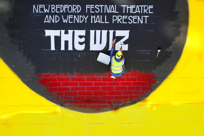 Mandy Fraser paints The Wiz  introduction next to a yellow brick road on Purchase Street in New Bedford, MA in front of the Zeiterion Theater for the production opening on April 27th, as seen from the roof of the Z. PHOTO PETER PEREIRA