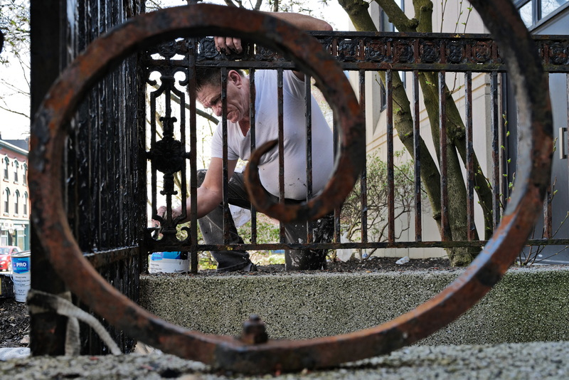 Marcos Rochas is framed by the ornate iron fence he is re-painting in front of the Union Square Office Center in New Bedford, MA.  PHOTO PETER PEREIRA