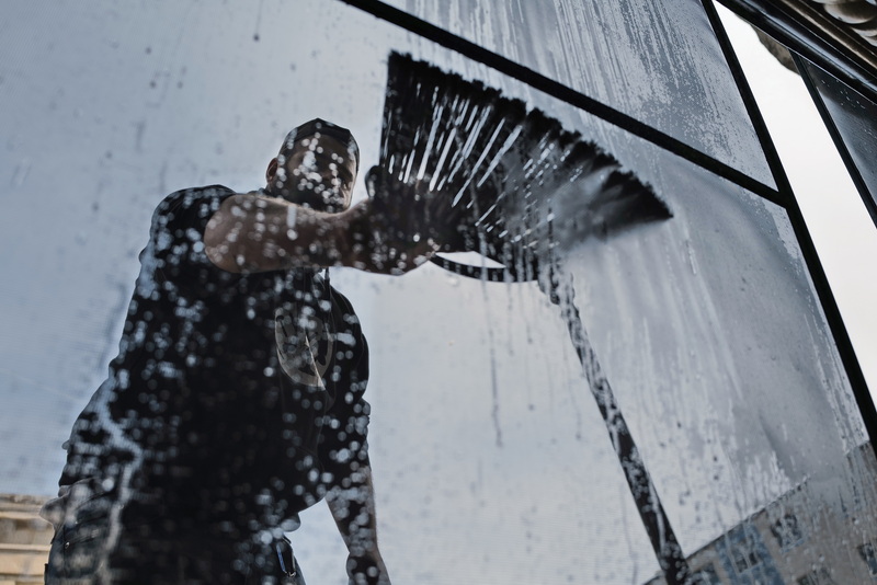 Zack Mendoza uses a broom to wash the screens from the windows of a building he is cleaning in downtown New Bedford. PHOTO PETER PEREIRA