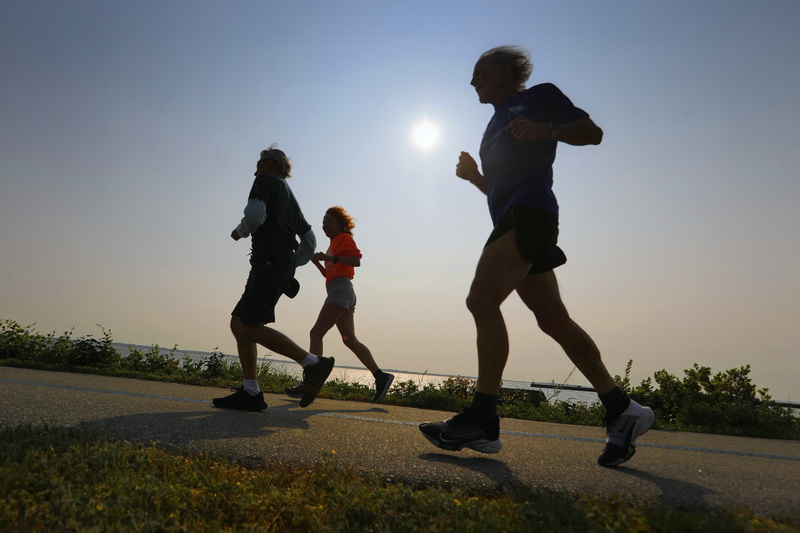 The sun rises in the distance as Peter Kenyon, Cheryl Healy and Don Cuddy go for a morning run around Fort Taber Park in New Bedford, MA. PHOTO PETER PEREIRA