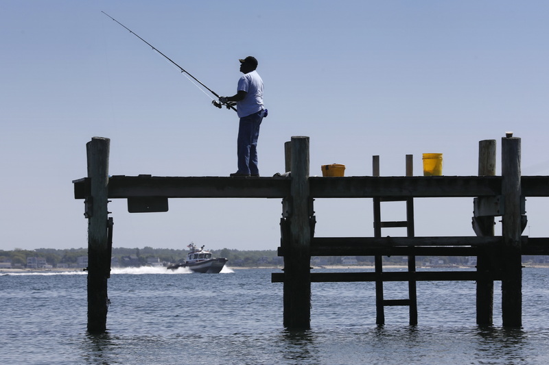 A man fishes from a dock in the south end of New Bedford, MA as a patrol boat makes its way out of the harbor in the distance. PHOTO PETER PEREIRA