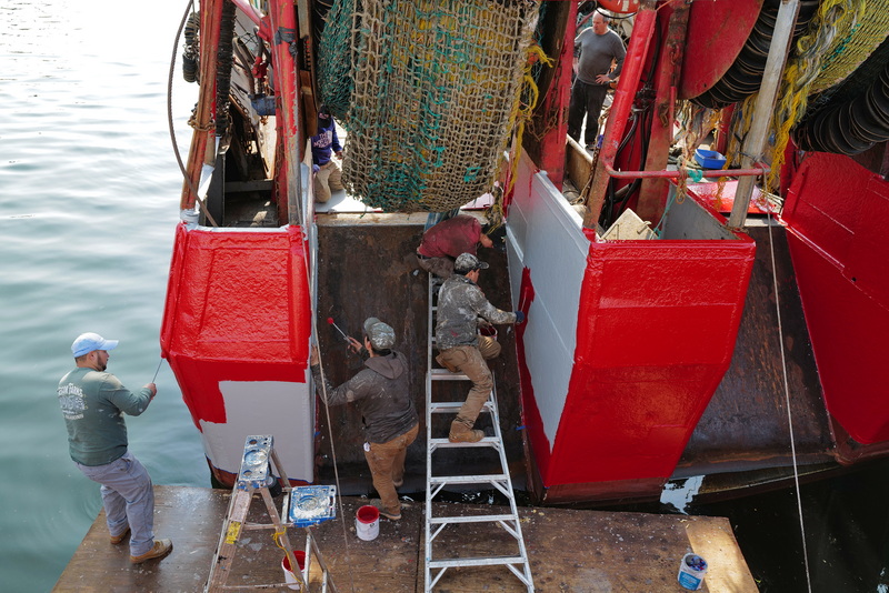 Owner of the fishing boat Fisherman, Pedro Cura, top right, looks on as painters put a fresh coat of red paint on his fishing boat docked in New Bedford, MA. PHOTO PETER PEREIRA