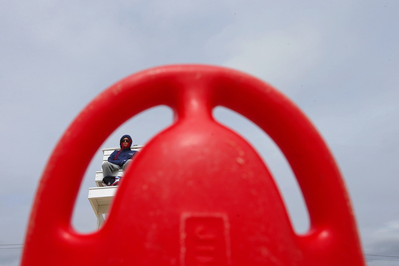 New Bedford lifeguard Tess Tarpey is seen through the gap on her rescue buoy, as she sits on the East Beach lifeguard station on a cloudy day. PHOTO PETER PEREIRA