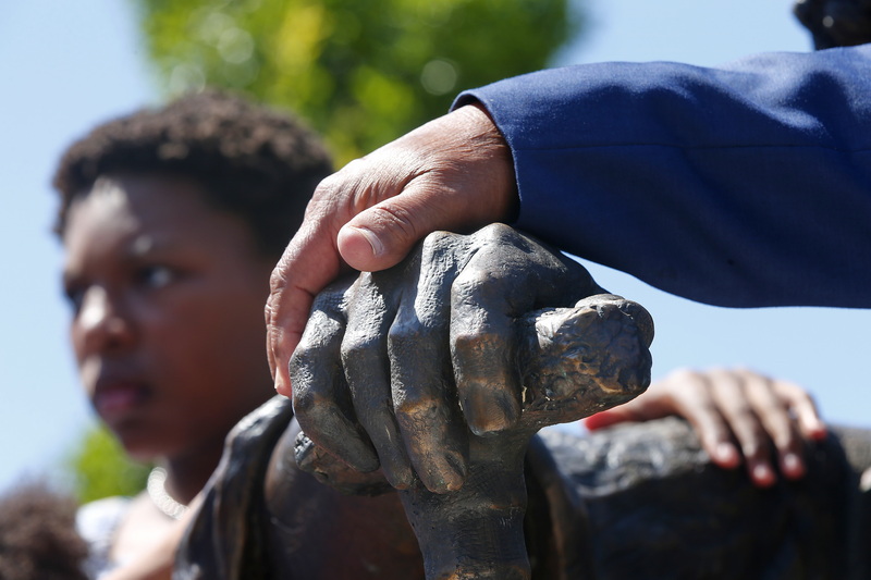 Richard Blake, sculptor, places his hand over the hand of the statue he made of Frederick Douglass, while in the background a boy holds the statue himself during the unveiling of the Douglass Memorial at the Abolition Row Park dedication in New Bedford, MA. PHOTO PETER PEREIRA