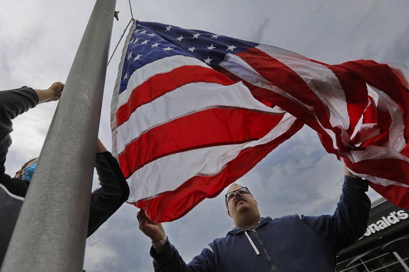 George Harrington, manager, gets a hand from Wilson Marcellino, left, installing a new larger five-by-eight foot American flag in front of the Fairhaven McDonald's in preparation for the fourth of July. PHOTO PETER PEREIRA