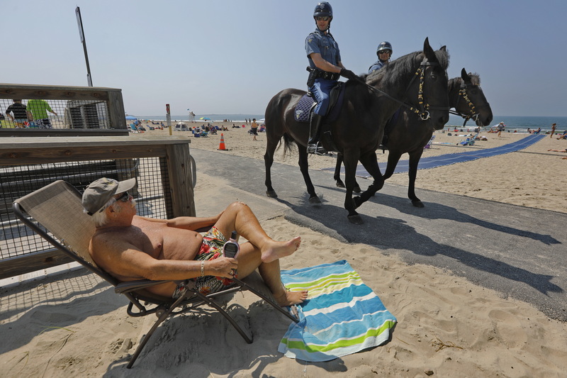 Massachusetts State Police Mounted Unit officers Alex Kisla and Jose Rodriguez ride past a sunbather at Horseneck Beach in Westport, MA as temperatures begin to climb across the region. PHOTO PETER PEREIRA