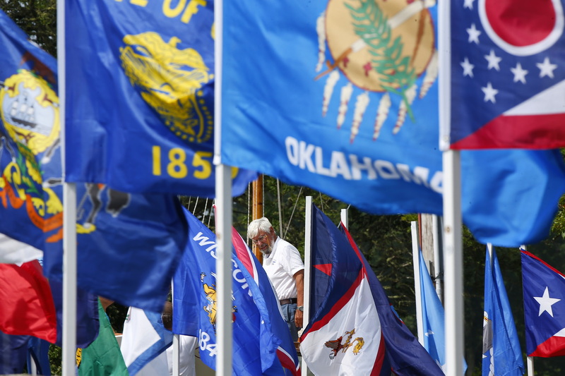 Ray Cullum gives his friends a hand in rigging their sailboat as seen through the State flags installed at Old Landing Wharf park in Marion, MA. PHOTO PETER PEREIRA