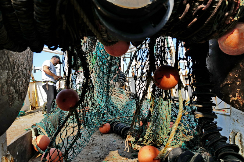 Antonio Cravo, captain of the fishing boat United States, makes repairs to the nets hanging down from the drum of the New Bedford,MA dragger, before heading back out to sea. PHOTO PETER PEREIRA