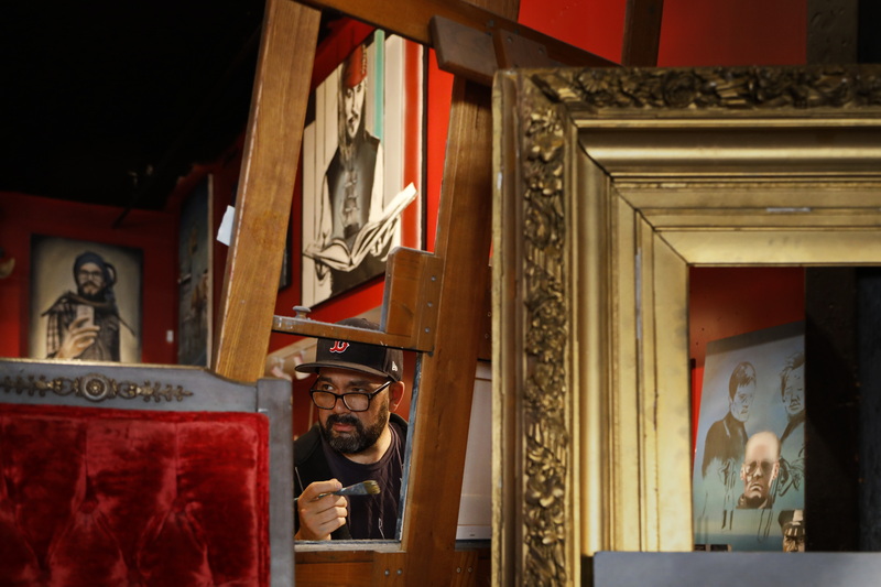 Ryan Mcfee and various paintings of his hanging on the walls, are framed by the easel and frame, as he works on a new painting at his studio/gallery on William St. in downtown New Bedford, MA.  PHOTO PETER PEREIRA