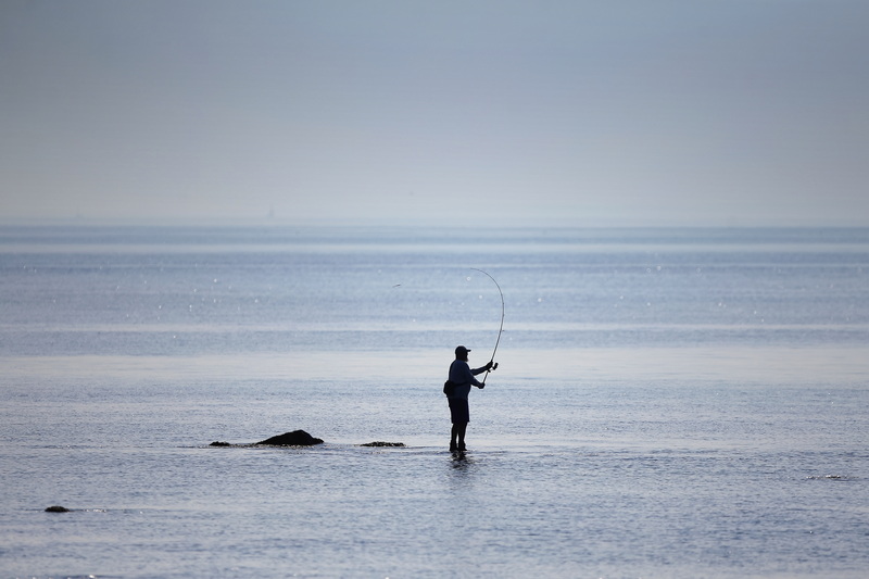 A man casts his line from a rock off of East Beach in Westport, MA on a hot calm morning.  PHOTO PETER PEREIRA