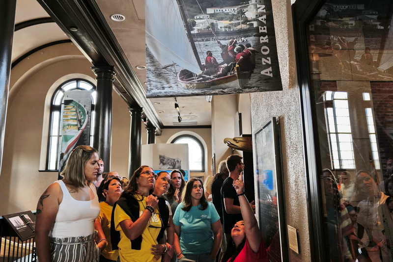 Lisa Lemieux, AMHS Womens Teams Captain, points to the photo of a previous Azorean Whaleboat Regatta as rowers from the Azorean islands of Pico and Faial who came to row in the Azorean Whaleboat Regatta in New Bedford visited the Whaling Museum as part of their tour of local culture.  PHOTO PETER PEREIRA