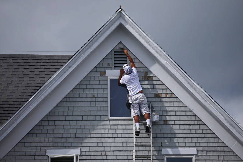 A painter paints the top of the roof gable of a home getting a fresh coat of paint in Mattapoisett, MA.  PHOTO PETER PEREIRA