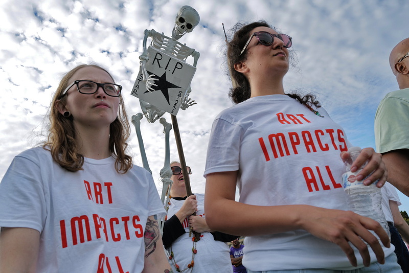 UMass Dartmouth ceramics students, Fallon Navarro and Anis Beigzadeh listen to speakers, while behind them assistant professor, Crystal Lubinsky, holds a skeleton with during a protest the closing of the Center of Visual and Performing Arts Center Star Store campus in downtown New Bedford. PHOTO PETER PEREIRA