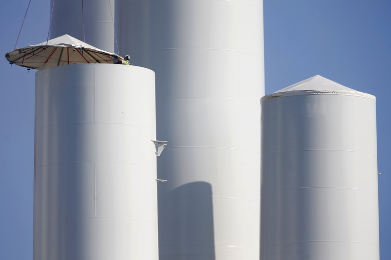 A worker is dwarfed by the giant towers as he installs a cover over one of the recently arrived wind turbine towers being assembled at the New Bedford Marine Commerce Terminal.  PHOTO PETER PEREIRA