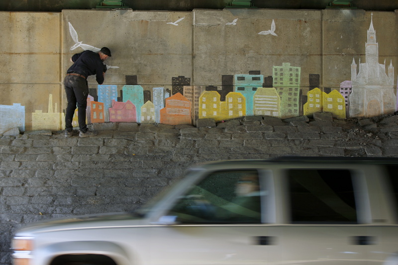 A motorist drives down MacArthur Drive past Manny Farias as he uses chalk to create a city scape under the Route 6 overpass in New Bedford, MA. PHOTO PETER PEREIRA