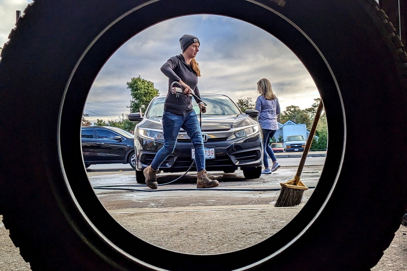 Molly McGee wraps up fixing a customer's flat tire at Joe's Tire in New Bedford, MA as seen through a new tire to be installed in another vehicle. PHOTO PETER PEREIRA