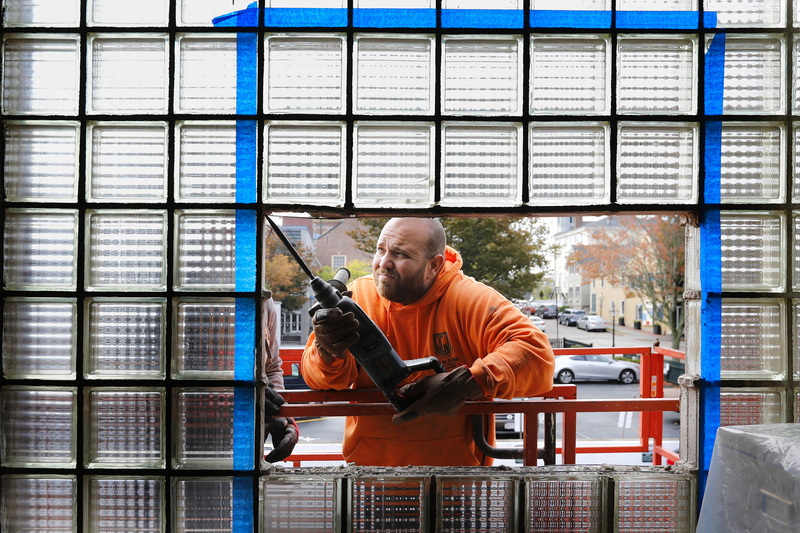 Jesse Camara removes the glass blocks from the outlined area at the Heritage Museum building in downtown New Bedford, MA to be filled by a conventional window PHOTO PETER PEREIRA