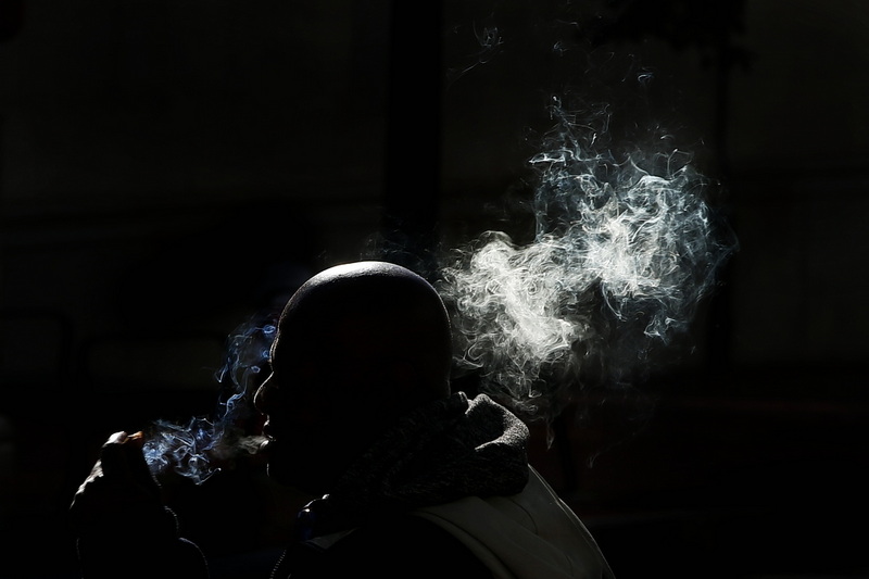 A man is cast in shadows by the buildings around him as he vapes a cigarette on Union Street in New Bedford, MA. PHOTO PETER PEREIRA