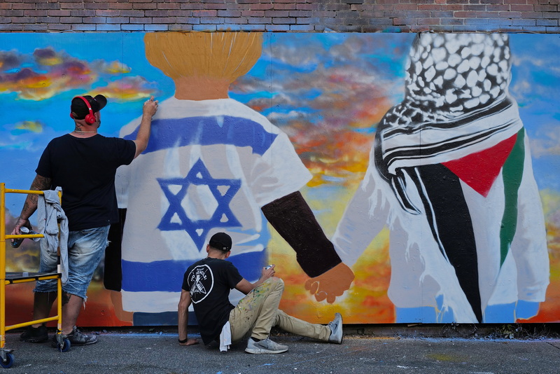 Local artists David Guadalupe and Brian Tillett paint a mural at Wings Court in New Bedford, MA showing an Israeli child and a Palestinian child holding hands as the sun rises in the distance. PHOTO PETER PEREIRA