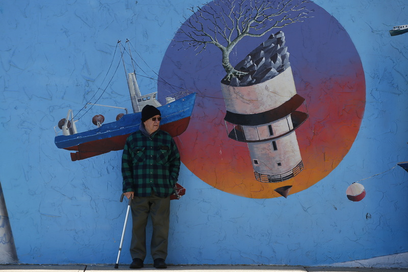 A man stands in front of a surreal mural painted on the wall of the Bank of America parking lot in New Bedford, MA. PHOTO PETER PEREIRA