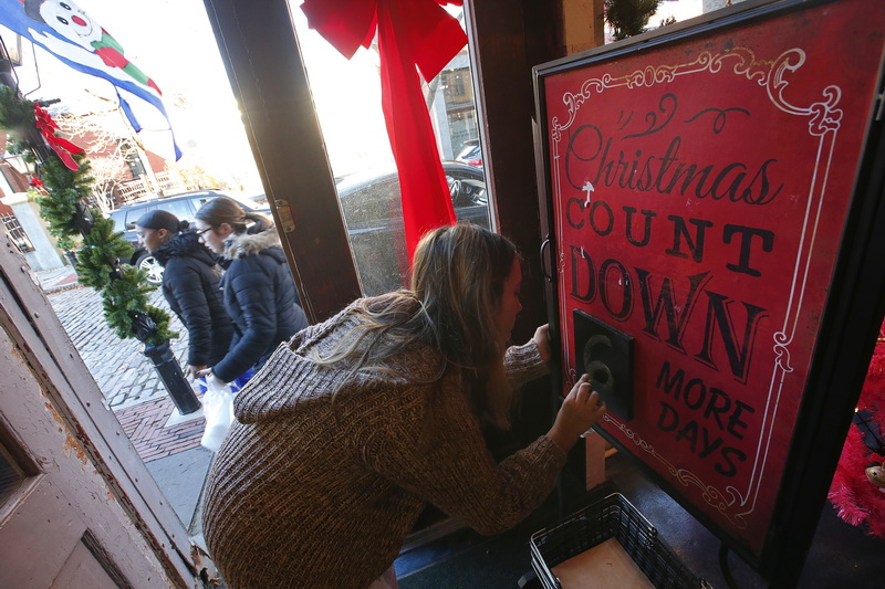 Chasitty Pacheco counts down the days to Christmas at a sign inside of the Bedford Merchant in downtown New Bedford, MA as two women walk up William Street, past the open front door.  PHOTO PETER PEREIRA