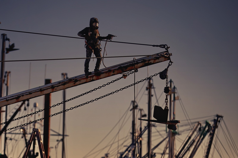 A painter looks ready for outer space exploration as he uses a pneumatic needle scaler to remove the rust from the outrigger of a fishing boat he is painting in New Bedford, MA. PHOTO PETER PEREIRA