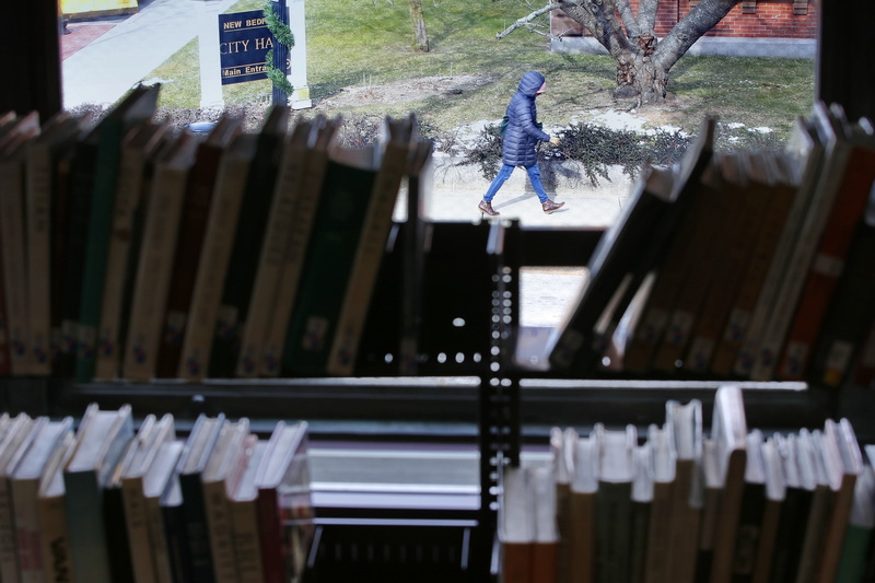 A woman makes her way to New Bedford City Hall as seen through a gap in the books at the New Bedford Public Library.  PHOTO PETER PEREIRA