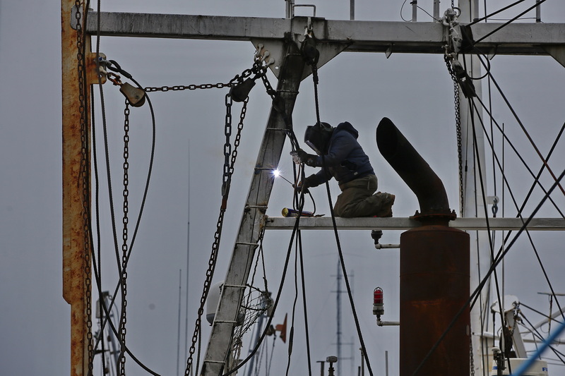 A welder finds himself high up making repairs to the mast of a fishing boat docked in New Bedford, MA.  PHOTO PETER PEREIRA