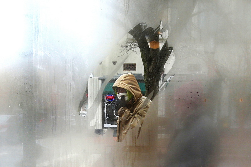 A man tries to keep his face warm as he makes his way across a gap in the steamed windows of No Problemo in downtown New Bedford, MA on a frigid morning. PHOTO PETER PEREIRA