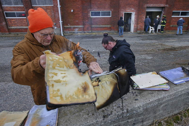 New Bedford firefighters are seen in the background as Roland Letendre, owner of the mill, and Kaylie Rutkowski, welder, attempt to salvage some, still on fire, documents from New England Water Jet Cutting, after a small explosion caused a fire inside of the business inside of a south end New Bedford, MA mill.  No injuries reported. PHOTO PETER PEREIRA